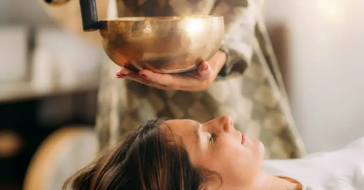 Benefits Of Sound Healing: a woman lies on her back and receives a singing bowl therapy
